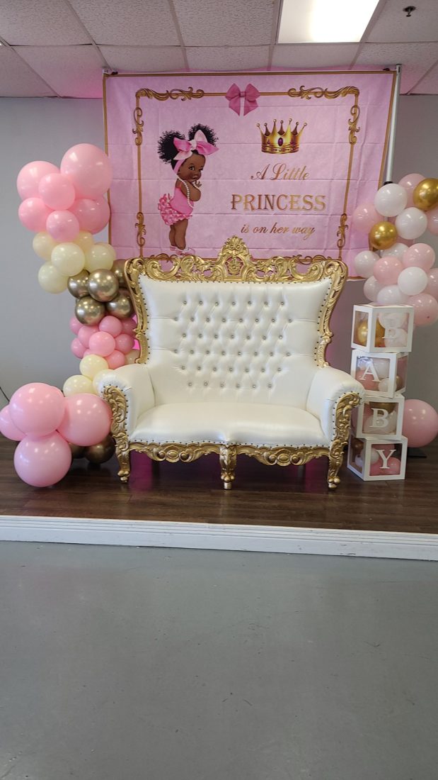 White and gold throne loveseat before a Little Princess backdrop, with pink, cream, and gold balloon columns and clear BABY blocks
